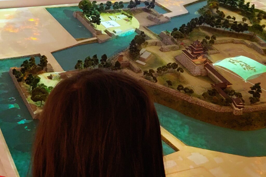 鶴ヶ城の展示室にある城下町のジオラマを見る娘。プロジェクションマッピングで光っている
